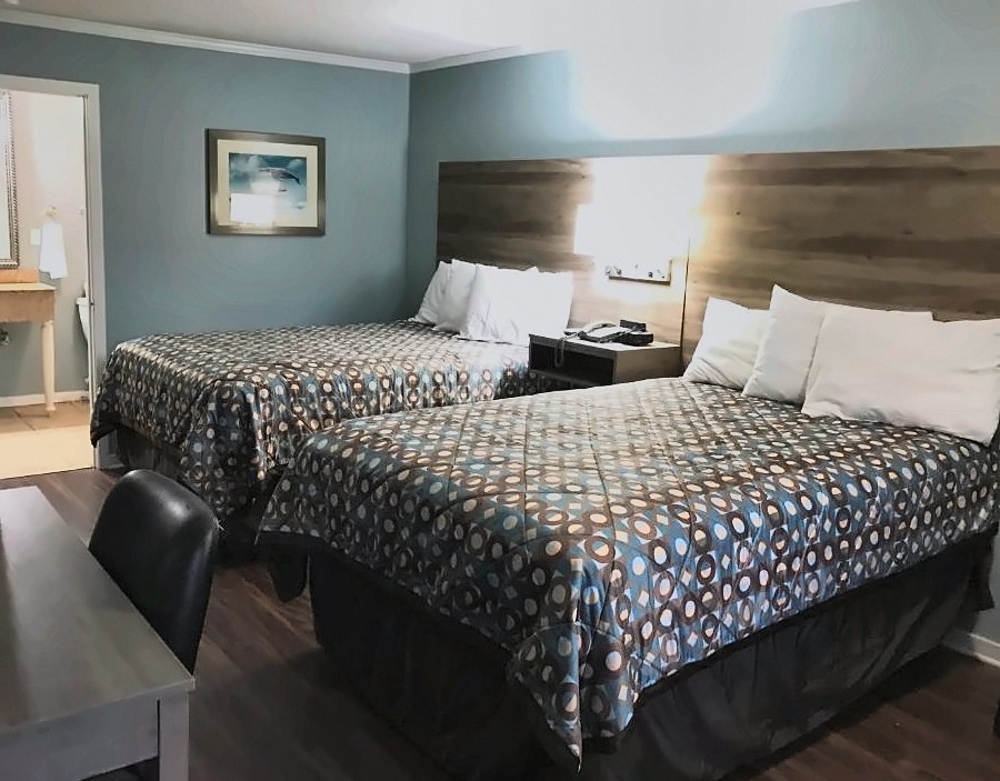 A guest room at Winton Inn & Suites with two beds, a desk and the bathroom vanity beyond